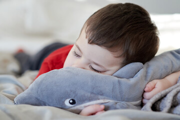 cute young boy taking a nap on the bed using his plush toy as a pillow - Powered by Adobe