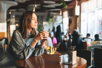 Young brunette woman wearing casual longsleeve enjoying her coffee sitting in cafe, city life