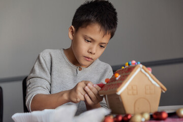 Lifestyle portrait of a boy decorating Gingerbread house at home, Christmas Holiday and childhood concept