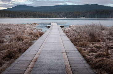 Obraz premium Wooden pier on lake site facing a beautiful mountain on a misty winter morning. Cold winters morning on a forest lake