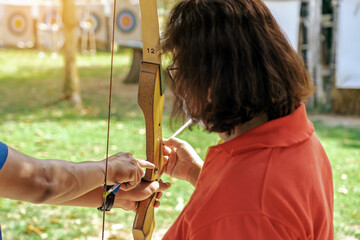 Female teacher teaches student to aim at goal. An archer teaching young man archery on field....