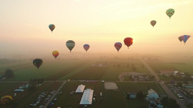 An Aerial View of Multiple Hot Air Balloons Rising into the Early Mist During a Festival With Crowds Watching, on a Summer Day