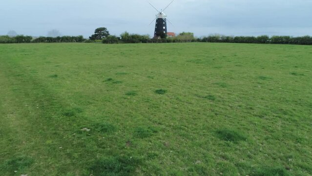 Rising Aerial Drone Shot Over Grass Field Towards Old Windmill Revealing Salt Marsh Behind in Burnham Overy Staithe North Norfolk UK