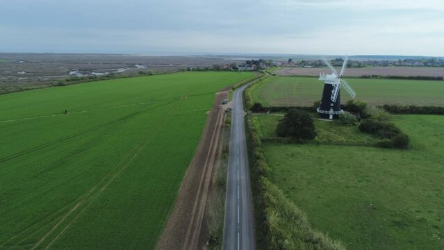 High Aerial Drone Shot Flying Down Road with Old Windmill with Fields and Marshes in Shot in Burnham Overy Staithe North Norfolk UK