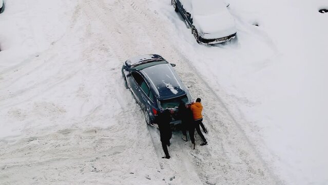 People are pushing a car out of snowdrifts in the courtyard of a house on the road. Ice under the snow on the road, winter tires. Windstorm