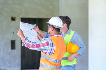Two construction engineers holding blue print and inspecting the construction site