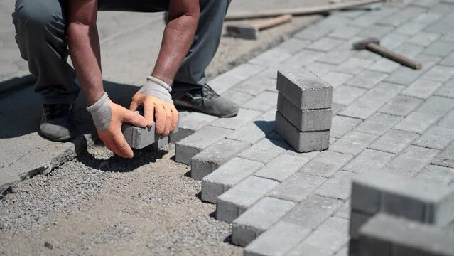 Worker laying gray concrete paving slabs on pavement, slow motion