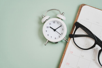 top view of white clock with  glasses on planner, and blurred hot coffee cup on a light green background including copy space. For planning business, working space concept