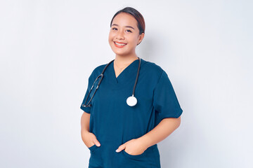 Smiling young Asian woman nurse wearing blue uniform with stethoscope holding hands in pockets...