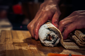 Japanese chef making California Maki Sushi with Masago - Roll made of Crab Meat, Avocado, Cucumber inside. Masago (smelt roe) outside with tuna, salmon, shrimp,traditional Japanese food ,Dark Tone