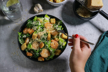close up of woman eating Cesar salad with fork on grey marble table