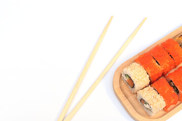 Delicious Japanese rolls with salmon, avocado, cucumber, cheese on wooden plate with wood sticks with selective focus on white background. Asian food concept. Healthy eating