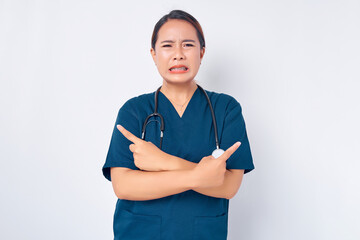 Sad Asian woman nurse wearing blue uniform with a stethoscope pointing fingers sideways left and...
