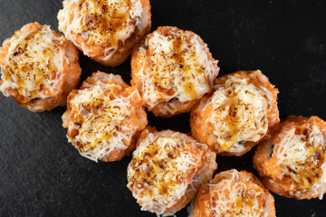 Hot sushi roll with cheese top. Baked sushi with seafood and crab, cream cheese topped on black background, top view.