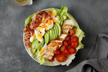 Cobb salad with bacon, avocado, tomato, grilled chicken, eggs on dark background. American salad....