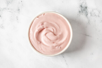 Yogurt with berries  in a white round saucer on grey background. Texture of white sour cream, ice cream. Curl of pink greek Yogurt.