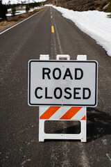 Road closed sign on mountain pass with snow in the background.  Vertical.  