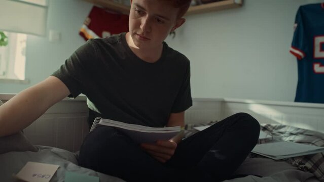 Tilt up of caucasian teenage boy sitting on bed and making notes. Shot with RED helium camera in 8K.   