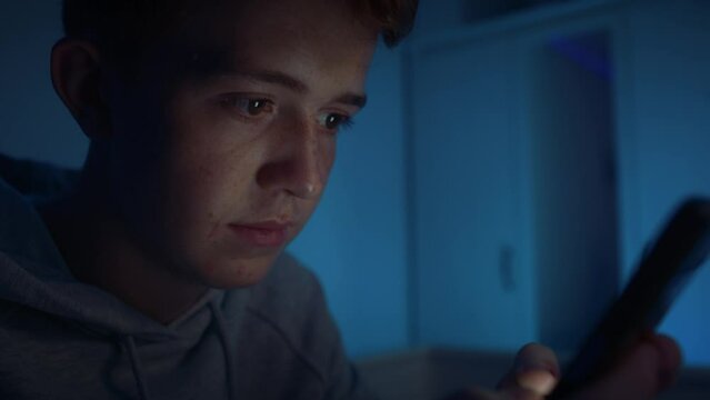 Caucasian teenage boy using mobile phone while sitting at night in his room. Shot with RED helium camera in 8K.    