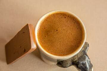 A cup of Turkish coffee on a beige tablecloth with milk chocolate next to it.