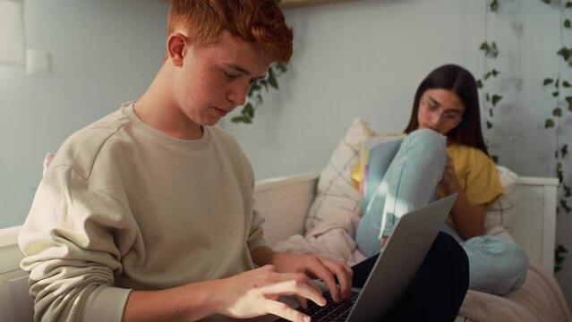 Two caucasian teenagers sitting on bed and learning from books and laptop in silence. Shot with RED helium camera in 8K.    