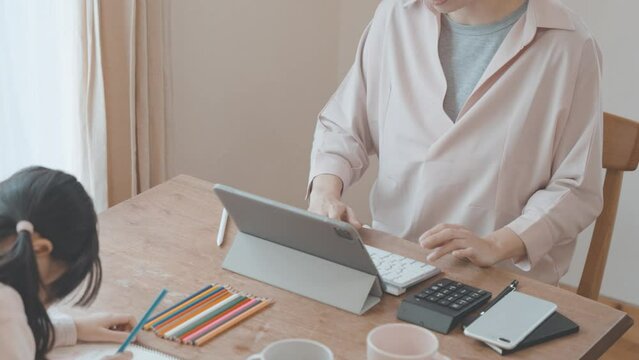 自宅でパソコンに向かう母親と、同じテーブルで遊ぶ女の子