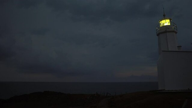 Lighthouse burning at dusk. Lighthouse light in rainy weather. Rotating lighthouse.