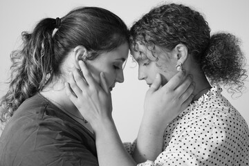 Zwei junge Frauen sind einander mit dem Gesicht zugewandt und halten sich mit den Händen am Gesicht