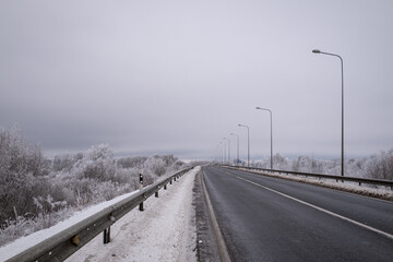 Fototapeta premium clean wet asphalt road in wintertime. Dirty snow on road sides. Long far perspective. Latvia landscape near Jelgava town. Bypass road 