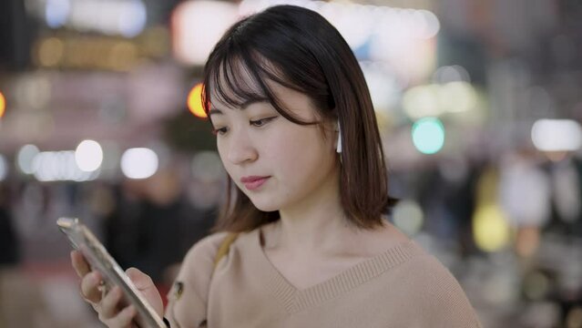 夜の繁華街でスマートフォンを見る若い女性