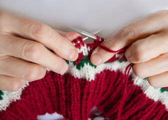 Close-up of an elderly woman's hands knitting a sweater with a pattern on the spokes