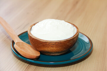 Fototapeta na wymiar White fermented milk yogurt in a decorative plate and wooden spoons on a brown background