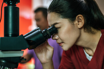 Asian young female farmer looking through a microscope in a laboratory. Modern technologies in agriculture management, agribusiness and research concept.