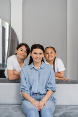 Smiling asian kids looking at camera near mother on couch at home