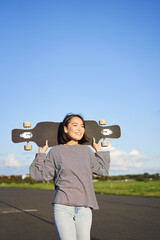 Vertical shot of carefree asian girl with longboard. Young woman skater holding cruiser on her...