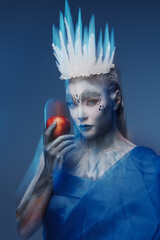 Studio shot of winter queen with frozen skin holding red apple.