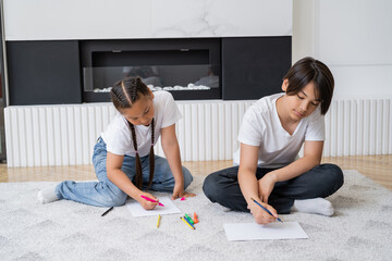 Asian siblings drawing on paper on carpet in living room