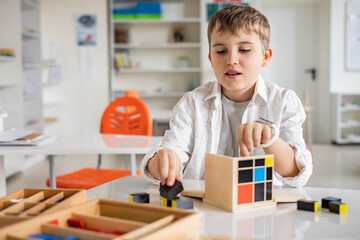 Happy male kid assembling Montessori material trinomial cube at school classroom desk