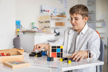 Happy male kid assembling Montessori material trinomial cube at school classroom desk