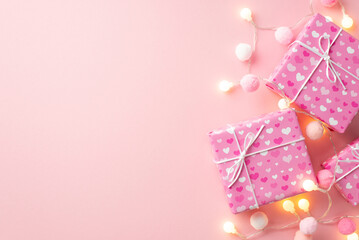 Valentine's Day concept. Top view photo of present boxes light bulb garland and soft pompons on isolated pastel pink background with copyspace