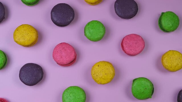 Rotating background of sweet macaroon cookies in different colors on a pink background