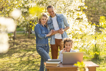 Naklejka premium little girl with mom and dad studying on laptop outdoor