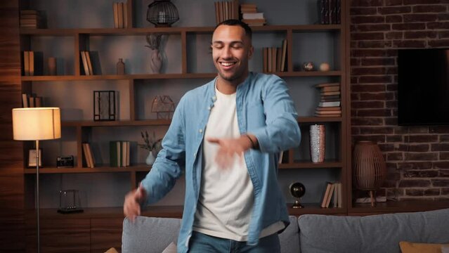 Active Carefree Young African American Man Enjoying Funny Dance Standing In Living Room, Happy Funky Independent Guy Dancing Having Fun Alone At Home Listening To Pop Music Moving Celebrating Freedom.