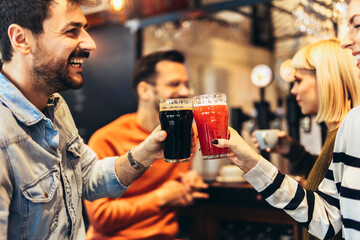Smiling young friends drinking craft beer in pub