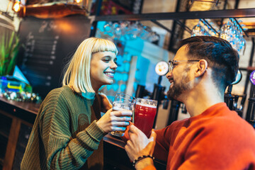 Smiling young couple at the bar with different varieties of craft beers toasting