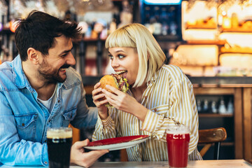 Young couple in love having fun spending leisure time together at restaurant, eating burgers and drinking beer