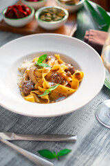 Pappardelle pasta with beef, gravy, parmesan and basil on a white plate. Italian dish served on a table, close up