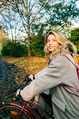 Young attractive caucasian woman ride on bicycle in the park on warm day in the fall.