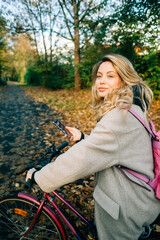 Fototapeta na wymiar Young attractive caucasian woman using mobile phone, ride on bicycle in the park on warm day in the fall.