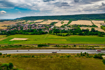 Naklejka premium Aerial bird view of typical Ardennes green field meadows and hill landscape also showing highway and buildings in te far background of this german environment. Germany.